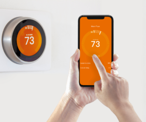 A person using a cell phone to control a smart thermostat.