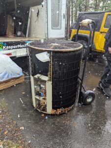 A dated, broken heat pump sitting outside a work truck while snow is falling.