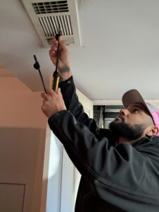 An HVAC technician checking airflow using a tool near a homeowner's ceiling air vent.